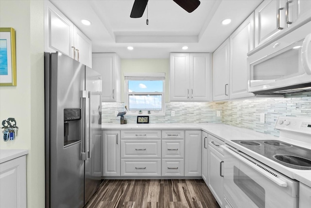 kitchen with decorative backsplash, white appliances, a raised ceiling, dark hardwood / wood-style floors, and white cabinetry