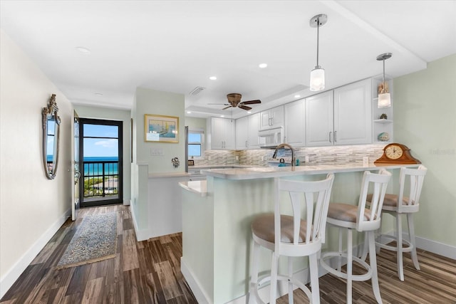 kitchen with kitchen peninsula, a kitchen breakfast bar, backsplash, and white cabinetry