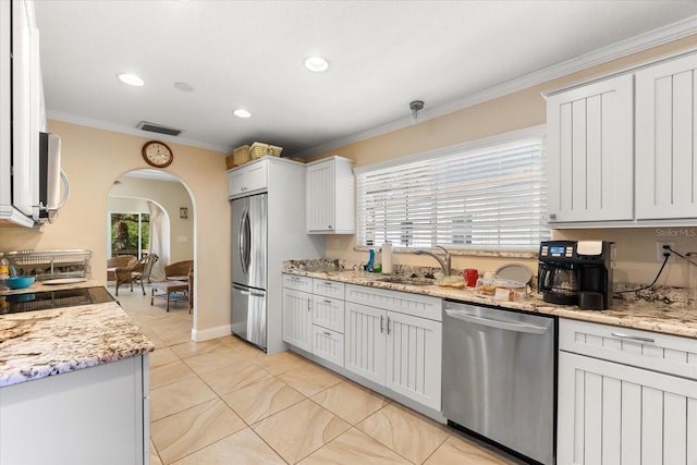 kitchen with appliances with stainless steel finishes, a healthy amount of sunlight, crown molding, sink, and white cabinets