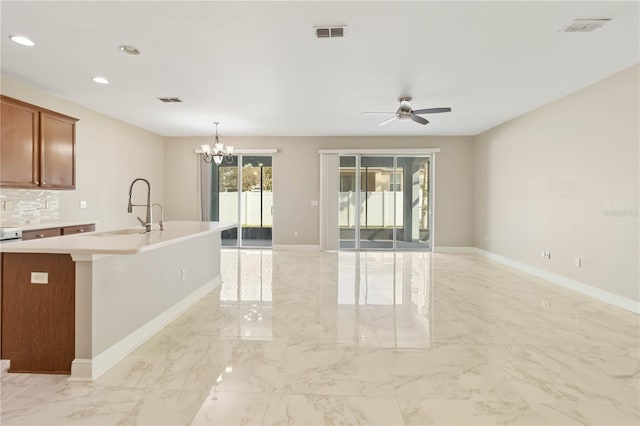 kitchen featuring sink, an island with sink, decorative light fixtures, decorative backsplash, and ceiling fan with notable chandelier