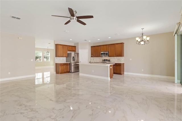 kitchen with ceiling fan with notable chandelier, stainless steel appliances, sink, pendant lighting, and an island with sink