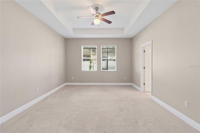 spare room featuring light carpet, a raised ceiling, and ceiling fan