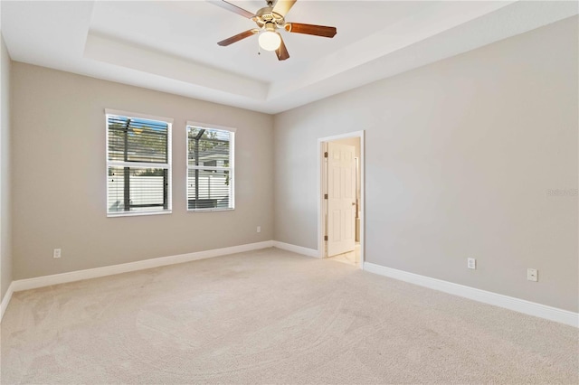 empty room with ceiling fan, light carpet, and a tray ceiling