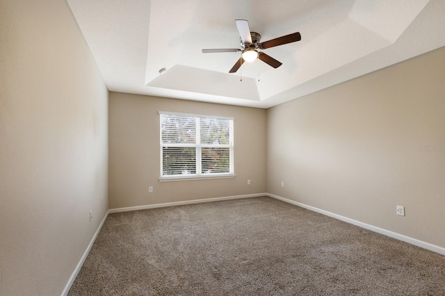 empty room featuring ceiling fan, a raised ceiling, and carpet