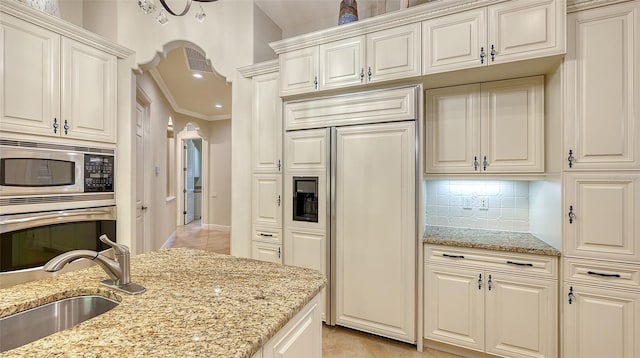 kitchen featuring light stone countertops, built in appliances, tasteful backsplash, and sink