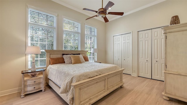 bedroom featuring light wood-type flooring, crown molding, ceiling fan, and multiple closets