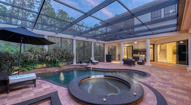 pool at dusk with glass enclosure, ceiling fan, an in ground hot tub, and a patio