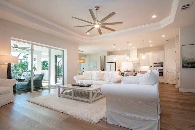 living room featuring a raised ceiling, crown molding, ceiling fan, and light hardwood / wood-style floors