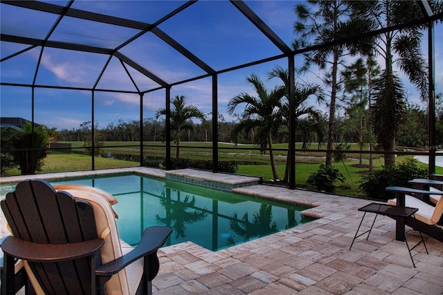 pool at dusk with glass enclosure, a yard, and a patio