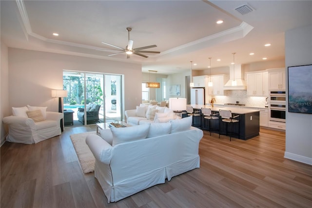 living room featuring a raised ceiling, ceiling fan, wood-type flooring, and ornamental molding