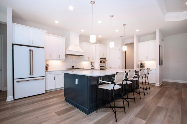 kitchen with white cabinets, appliances with stainless steel finishes, an island with sink, and custom exhaust hood