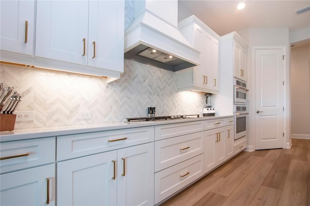 kitchen with premium range hood, tasteful backsplash, light hardwood / wood-style floors, white cabinetry, and stainless steel appliances