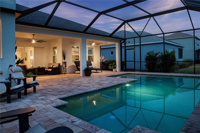 pool at dusk with a lanai, outdoor lounge area, ceiling fan, and a patio