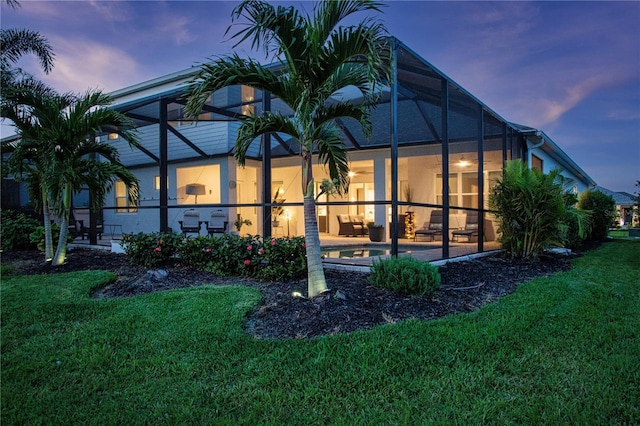 back house at dusk with a yard, glass enclosure, and a patio area