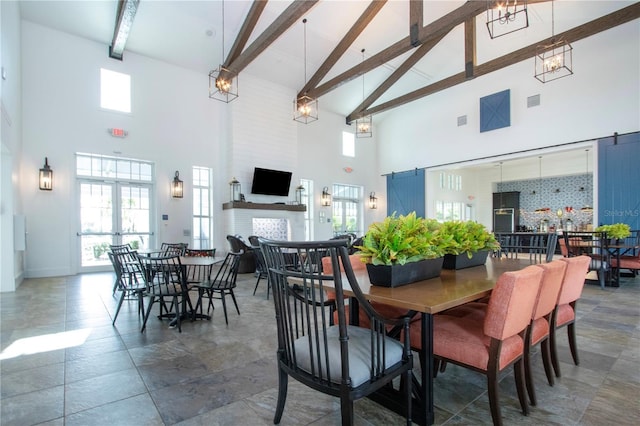 dining area with beamed ceiling, a high ceiling, and a large fireplace