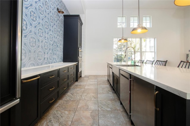 kitchen featuring sink, hanging light fixtures, crown molding, a center island with sink, and appliances with stainless steel finishes