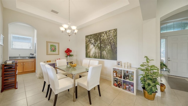 dining room with a notable chandelier, light tile patterned flooring, a raised ceiling, and a healthy amount of sunlight