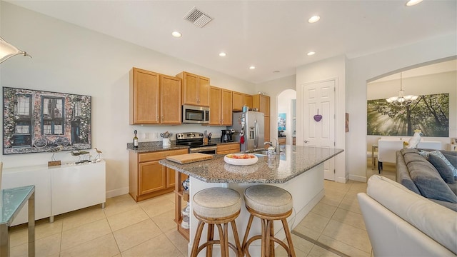 kitchen with an inviting chandelier, a breakfast bar area, dark stone countertops, light tile patterned floors, and stainless steel appliances