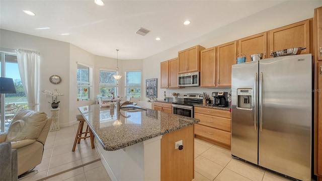 kitchen featuring appliances with stainless steel finishes, a center island with sink, light tile patterned floors, and decorative light fixtures