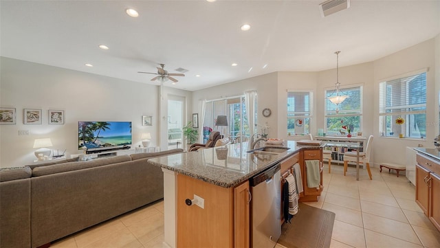 kitchen featuring ceiling fan, hanging light fixtures, light stone counters, stainless steel dishwasher, and a kitchen island with sink