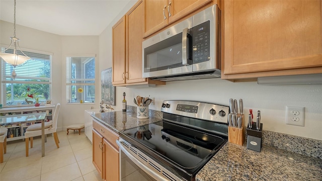 kitchen with pendant lighting, stainless steel appliances, light tile patterned floors, and dark stone countertops