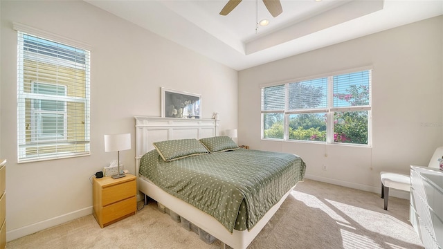 bedroom featuring ceiling fan, light colored carpet, and a tray ceiling