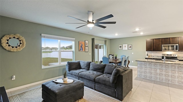 tiled living room featuring a water view, ceiling fan, and sink