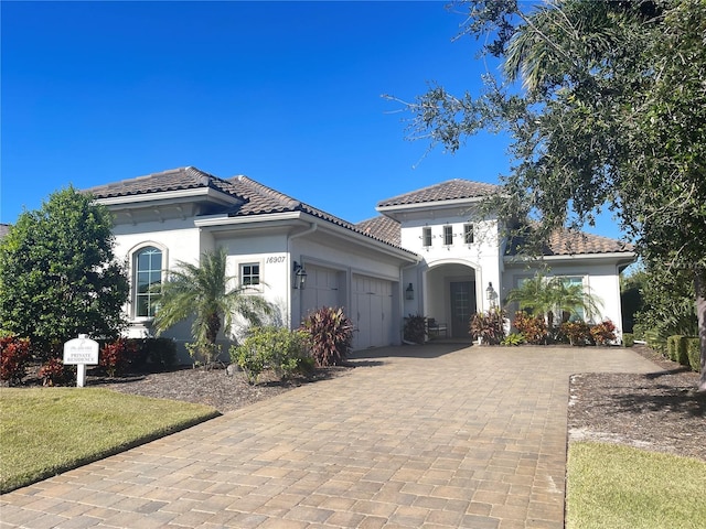 mediterranean / spanish-style home featuring a garage, decorative driveway, a tiled roof, and stucco siding