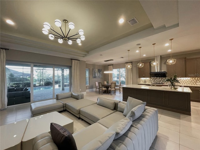 tiled living room featuring a tray ceiling and a chandelier