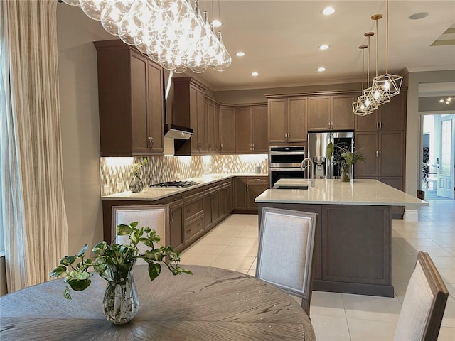 kitchen featuring decorative backsplash, stainless steel appliances, a kitchen island with sink, sink, and hanging light fixtures