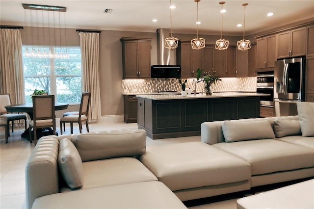 kitchen with appliances with stainless steel finishes, pendant lighting, wall chimney exhaust hood, and an island with sink