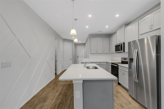 kitchen featuring a sink, light countertops, appliances with stainless steel finishes, an island with sink, and decorative light fixtures