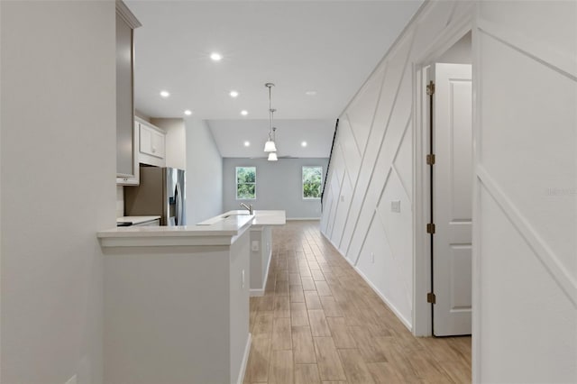 kitchen with white cabinets, stainless steel fridge with ice dispenser, hanging light fixtures, light countertops, and light wood-style floors