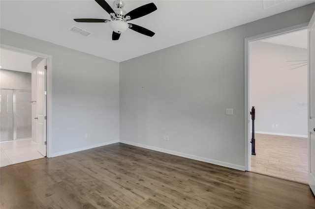 spare room featuring a ceiling fan, visible vents, baseboards, and wood finished floors