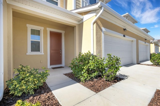 entrance to property featuring driveway, an attached garage, and stucco siding