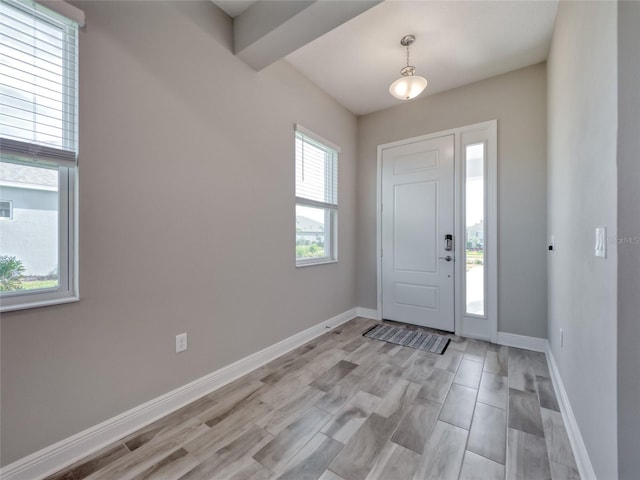 entryway featuring beamed ceiling, light wood-style flooring, and baseboards