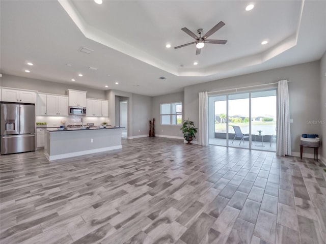 unfurnished living room featuring baseboards, a raised ceiling, a ceiling fan, light wood-type flooring, and recessed lighting