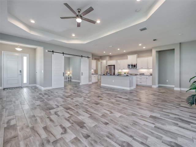 unfurnished living room with light wood-style floors, a barn door, visible vents, and a tray ceiling