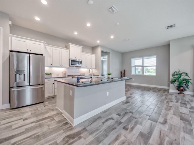 kitchen featuring visible vents, white cabinetry, appliances with stainless steel finishes, dark countertops, and a center island with sink