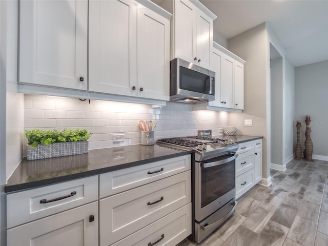 kitchen with baseboards, decorative backsplash, dark stone counters, appliances with stainless steel finishes, and white cabinetry