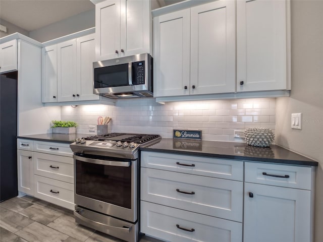 kitchen with dark countertops, white cabinets, stainless steel appliances, and backsplash