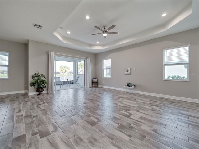 unfurnished room with light wood-style floors, a tray ceiling, visible vents, and baseboards