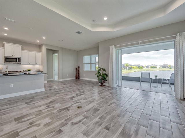 unfurnished living room featuring baseboards, visible vents, a water view, a tray ceiling, and recessed lighting