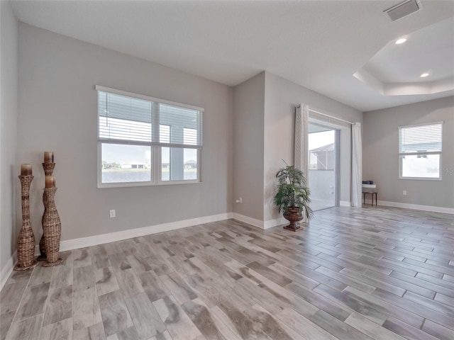 unfurnished living room with light wood-type flooring, a raised ceiling, visible vents, and baseboards