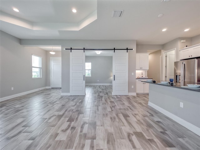 unfurnished living room with light wood-type flooring, a wealth of natural light, visible vents, and a barn door