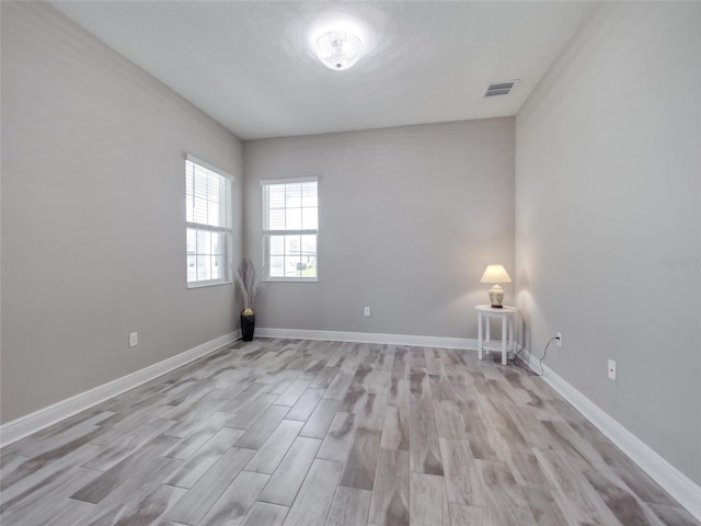 empty room featuring light wood-style floors, visible vents, a textured ceiling, and baseboards