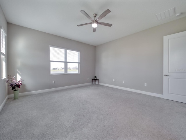 empty room featuring visible vents, light colored carpet, a ceiling fan, and baseboards