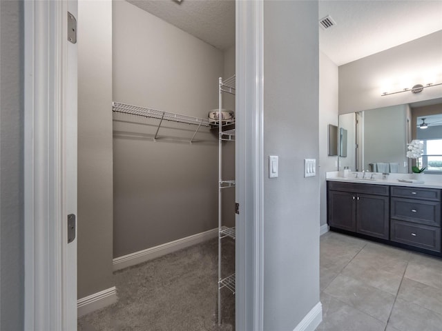 bathroom with a spacious closet, vanity, visible vents, and baseboards