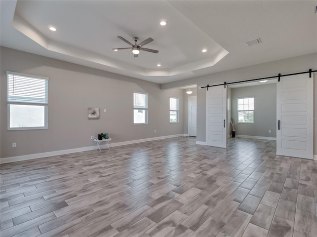 unfurnished living room featuring ceiling fan, a barn door, visible vents, baseboards, and a tray ceiling