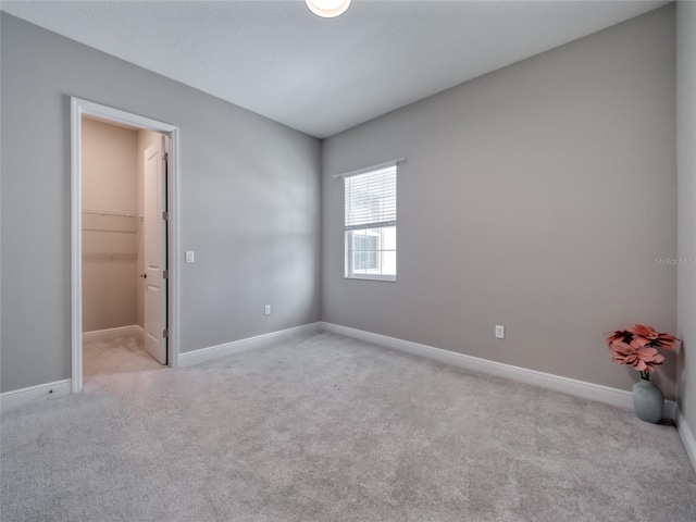 unfurnished bedroom with a walk in closet, light carpet, and baseboards